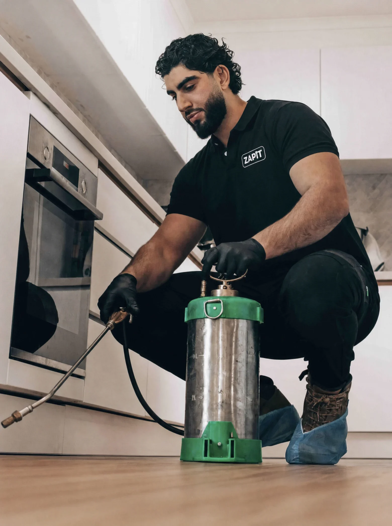 A Zap It technician kneeling with a pressure sprayer in a kitchen