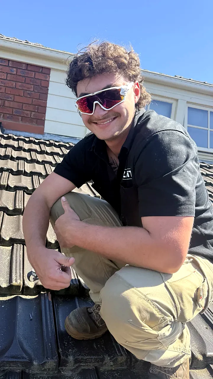 Rudy, Pest technician at Zap It, crouching on a tiled roof, smiling