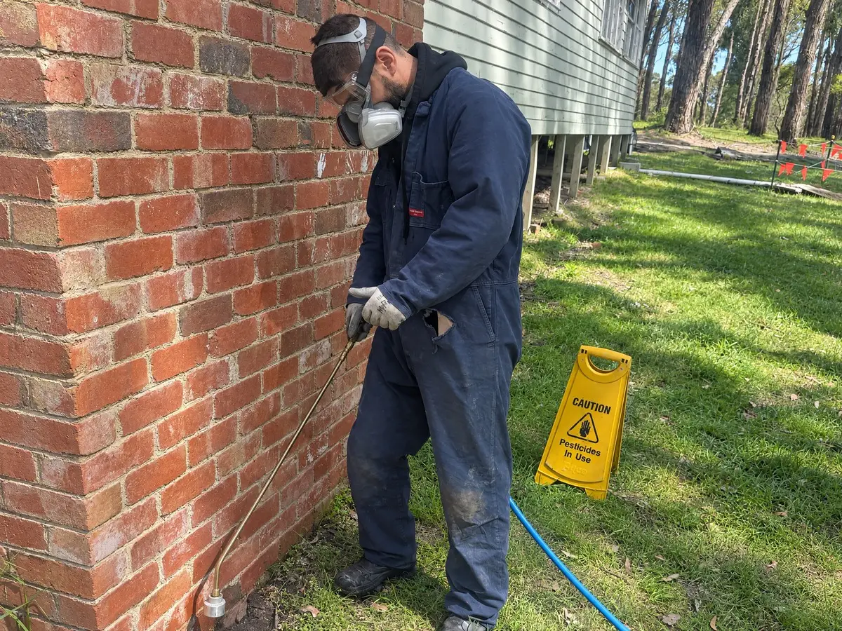 Zap It technician applying a liquid termite barrier at the base of a brick wall